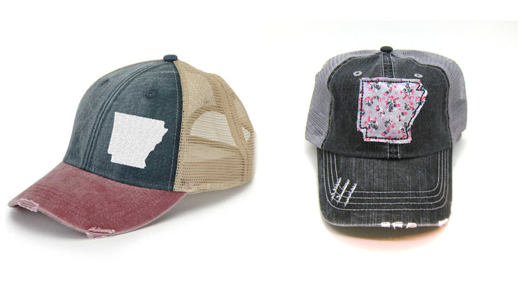 photo of a navy and burgundy trucker hat with silhouette of arkansas in white and gray trucker hat with gray floral distressed patch of arkansas